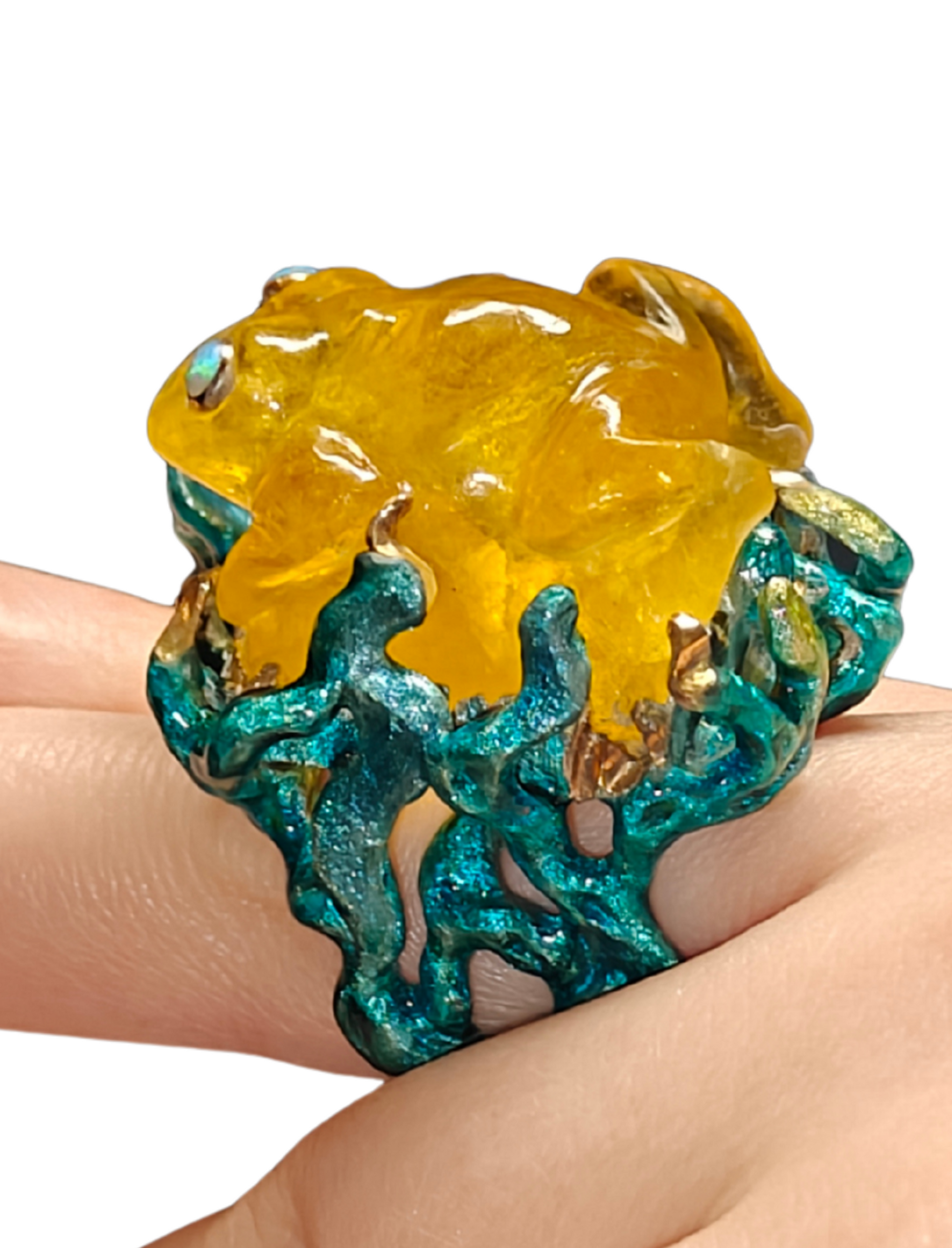 Close-up of the Kelp Dancer ring worn on a hand from the Stone Garden Collection by Konforti Jewelry, handcrafted in 960 silver and crowned with a 100 ct yellow lepidolite carved as a frog, featuring opal eyes and hand-painted Limoges enamel inspired by underwater kelp.