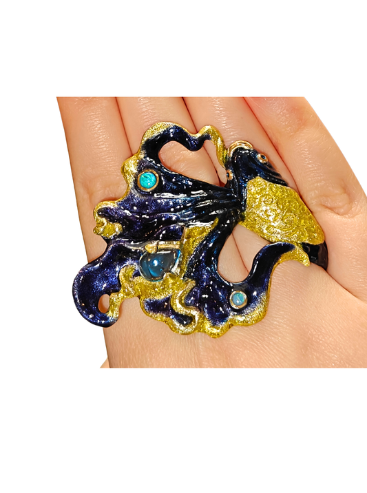 Close-up of the Ocean Duet ring worn on a hand from the Stone Garden Collection by Konforti Jewelry, handcrafted in 960 silver and adorned with 3 ct blue topaz and 0.01 ct opal gemstones, featuring hand-painted Limoges enamel that evokes ocean waves and movement.