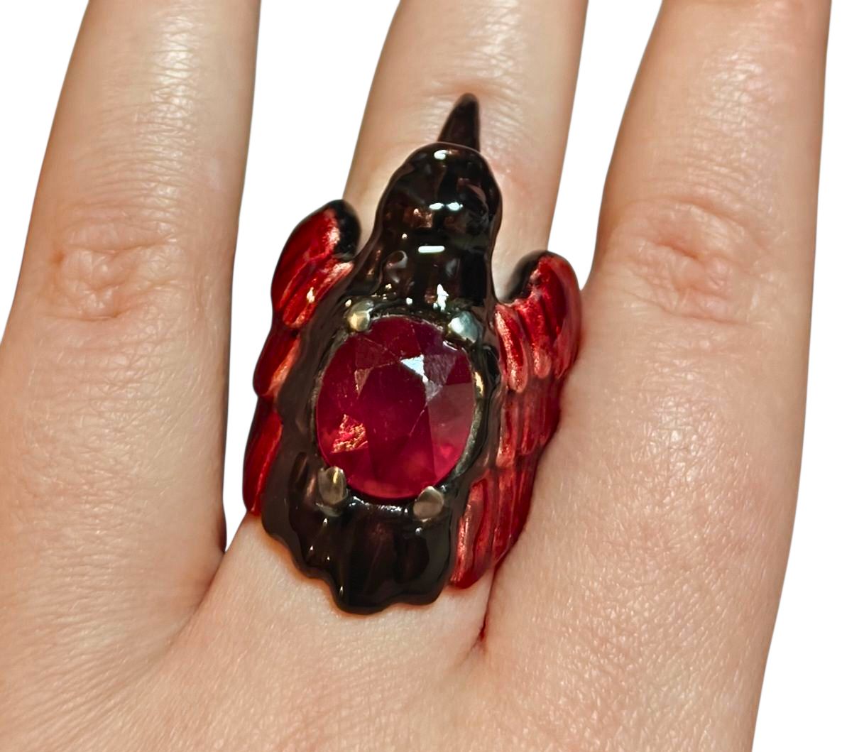 Close-up of the Royal Raven ring worn on a hand from the Stone Garden Collection by Konforti Jewelry, showing the 8.45 ct treated ruby centerpiece, 960 silver craftsmanship, and fine Limoges enamel with 24K gold-plated accents evoking the majesty of a raven in flight.