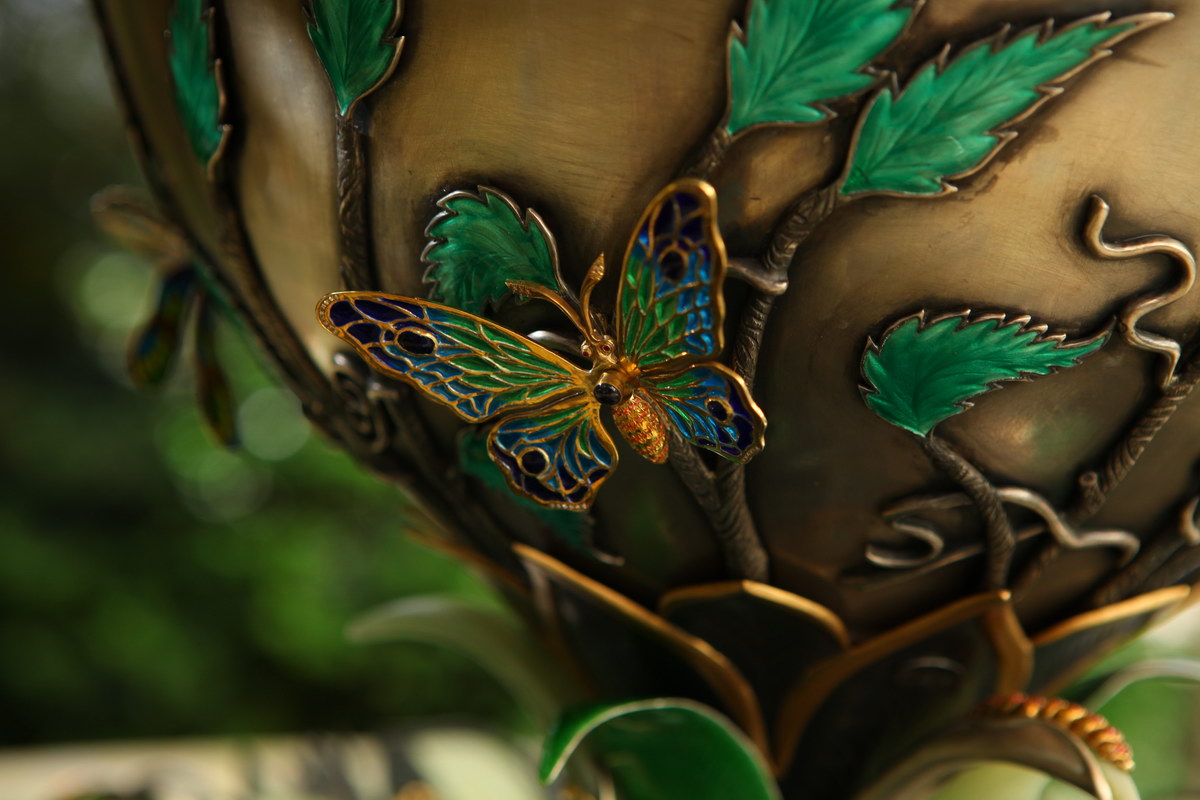 Lifestyle close-up of a butterfly in hot enamel on the vase of the “Summer Pond” centerpiece, emphasizing translucency, craftsmanship, and integration within the sculptural scene.