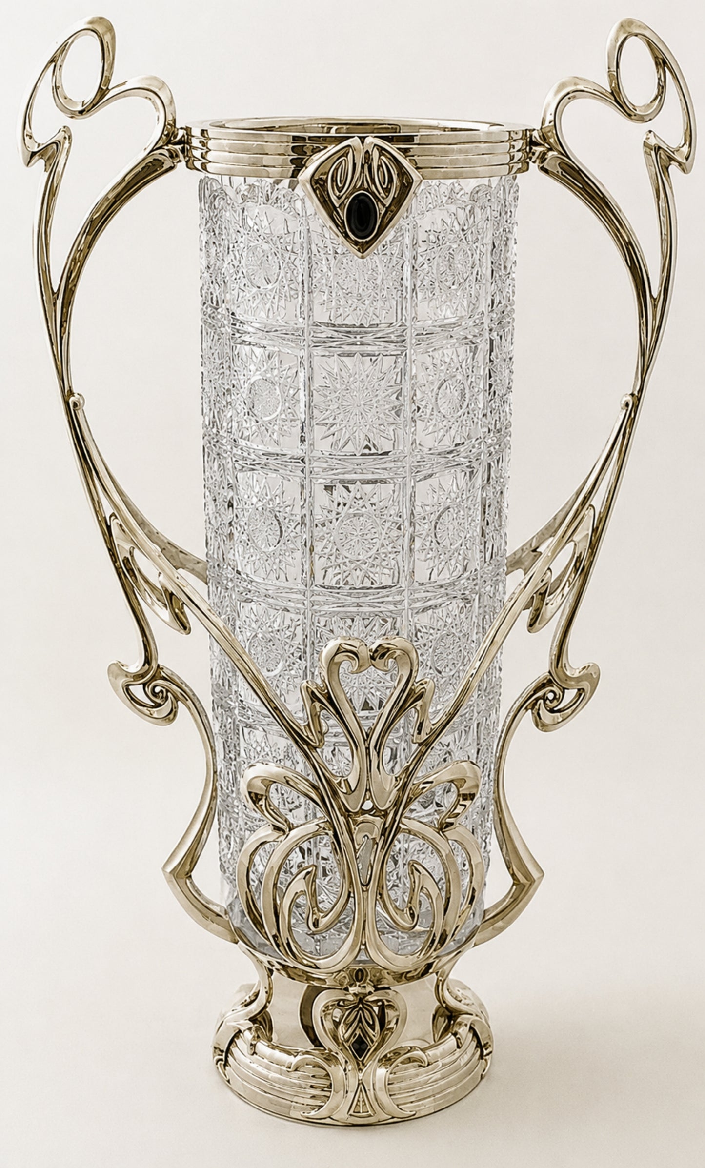 An ornate Art Deco style vase featuring a clear cut-glass cylindrical body and an elaborate silver-toned metal frame with scrollwork and a decorative base.