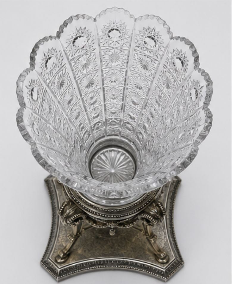 A cut crystal bowl with a decorative silver pedestal base, photographed against a neutral light gray background.
