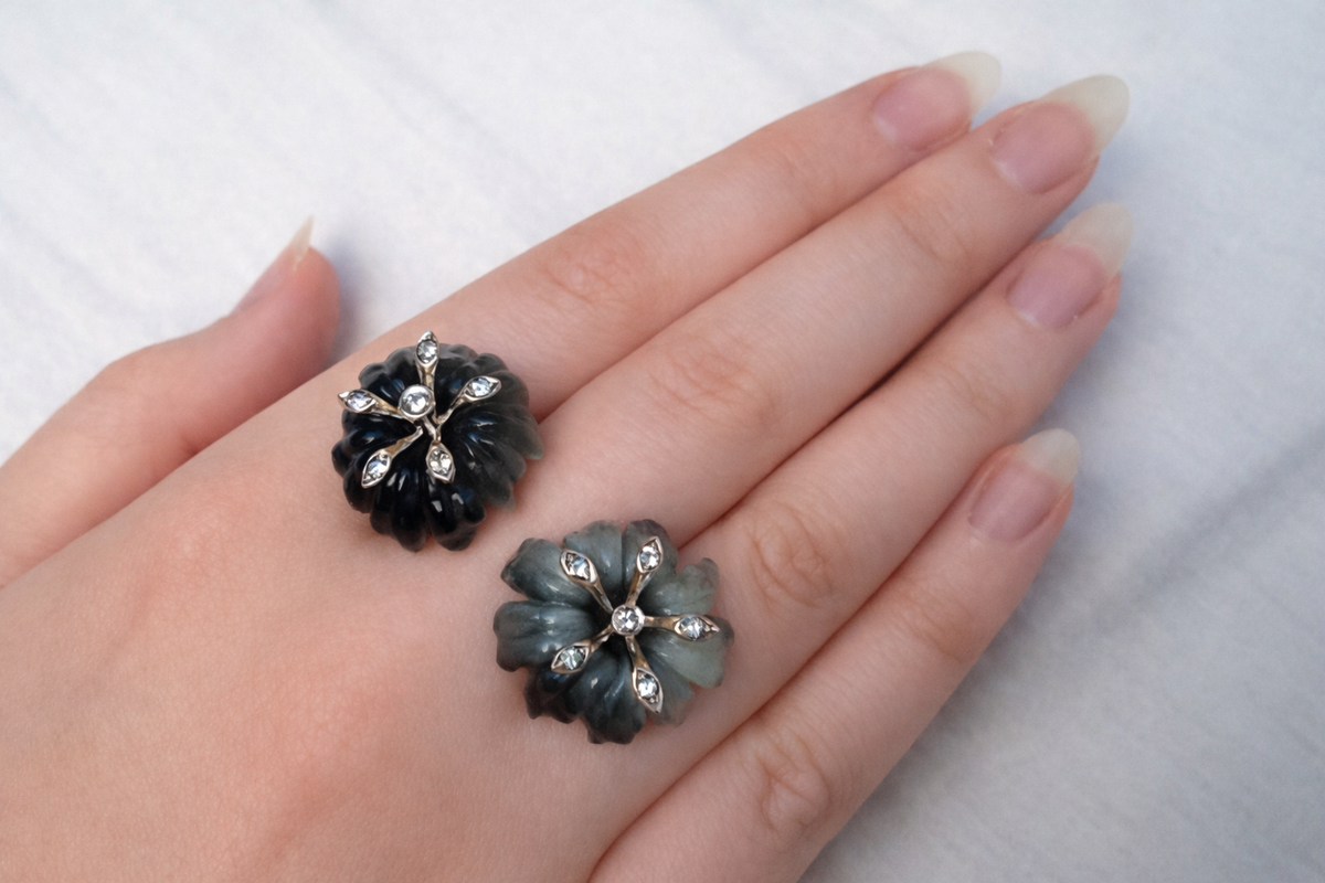 Hand-carved cat's eye lily cocktail ring in rhodium-plated 18K white gold with grey sapphires, shown in a close-up on a finger.