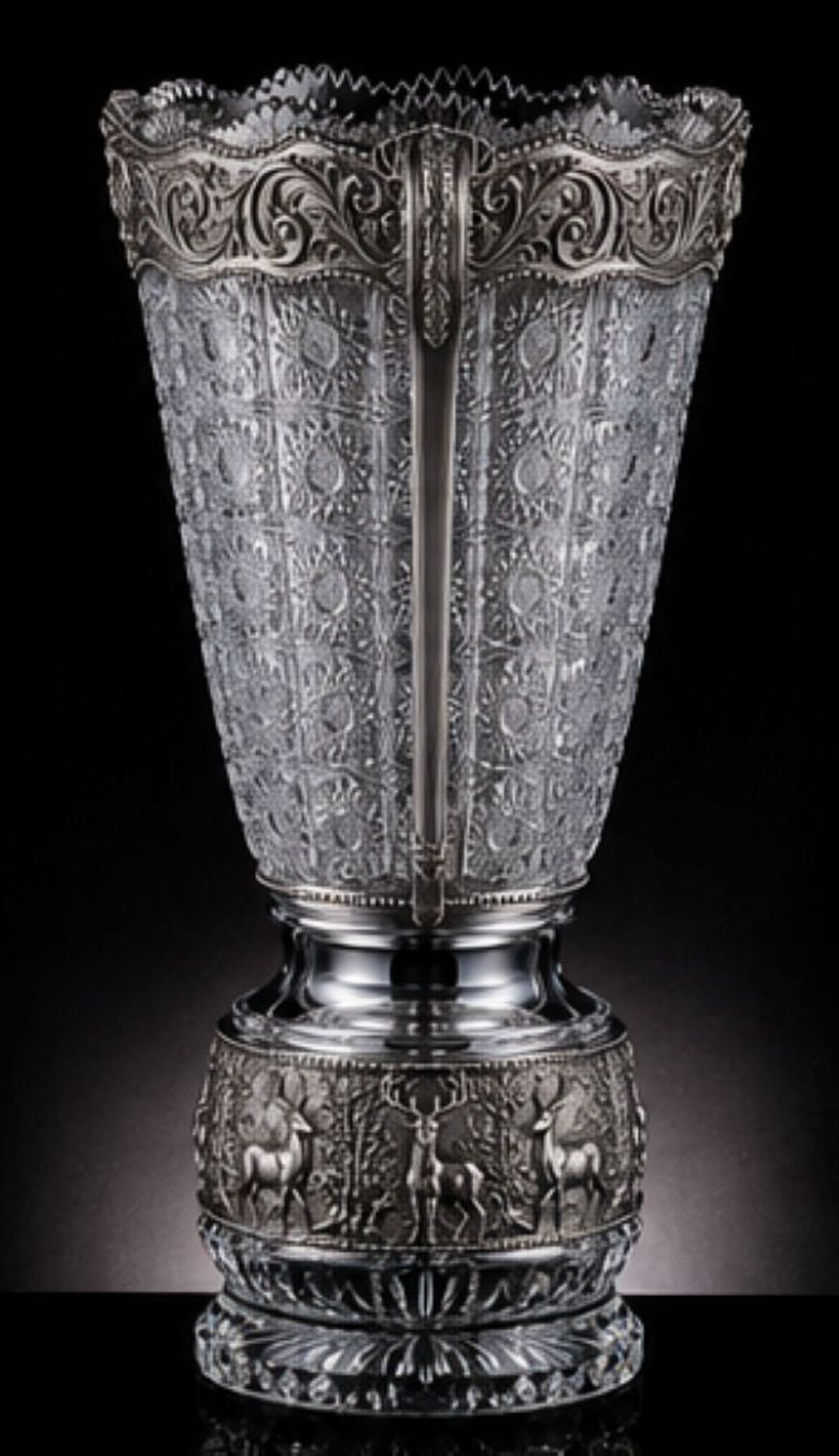 An ornate silver-toned crystal vase with a flared, embossed patterned body, a decorative band featuring deer relief, and a scalloped filigree rim, shown against a dark studio background.
