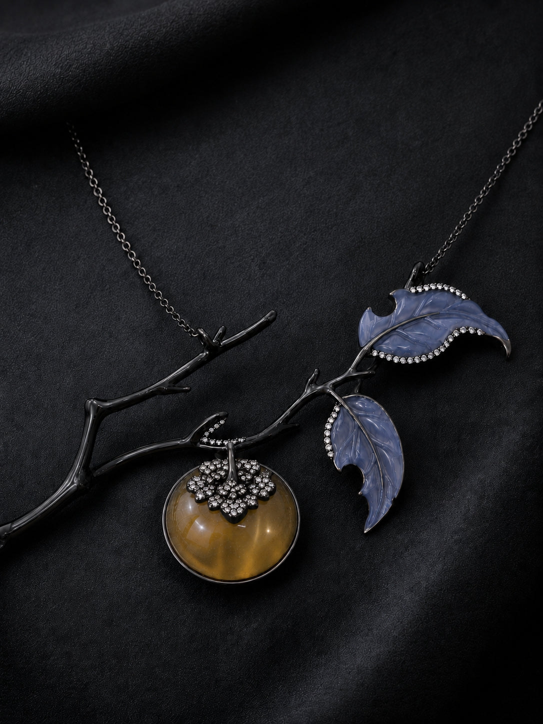 Luxury Golden Persimmon pendant displayed on black satin, handcrafted in black rhodium-coated 18K gold with carved lepidolite, angelite leaves, and pavé diamonds.