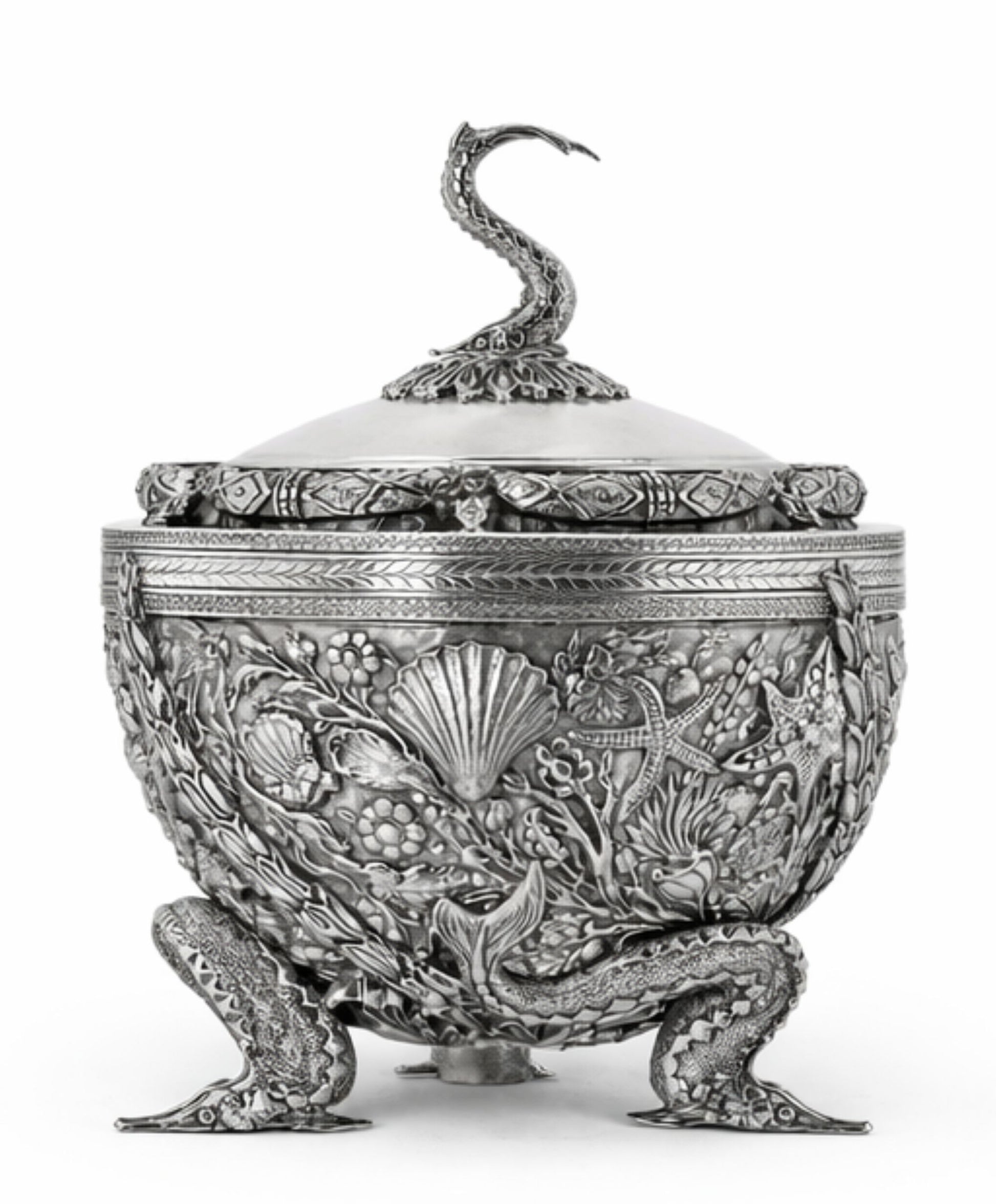 An ornate silver-toned lidded container or candelabra with intricate relief carvings of floral and marine motifs, featuring a sculpted snake handle on the lid and three detailed feet, shown against a plain white background.