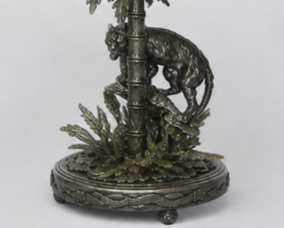 An ornate bronze-finished metal sculpture depicting a monkey climbing a bamboo pole, mounted on a decorative circular base with foliage details, photographed against a light gray background.