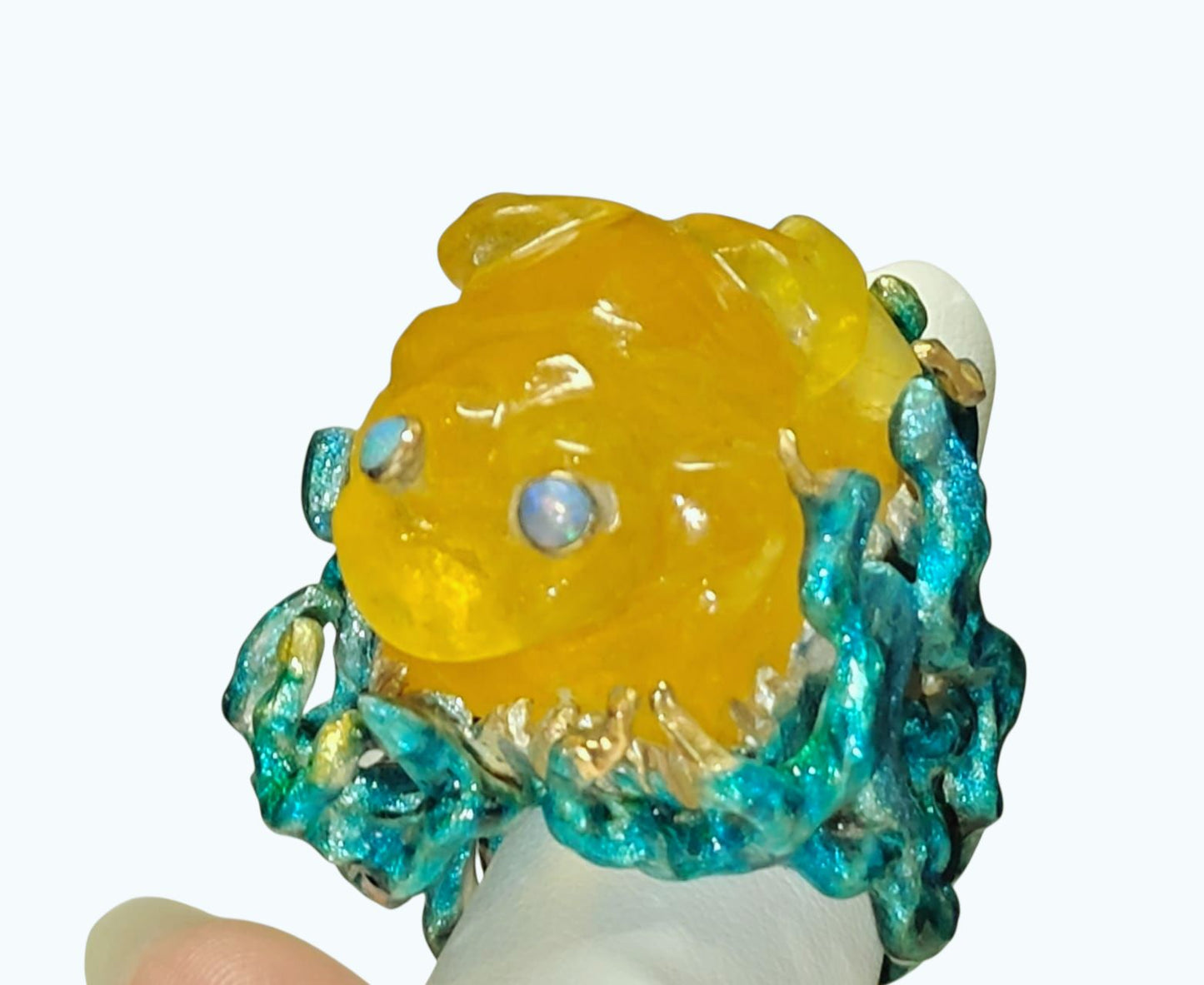 Top view of the Kelp Dancer ring on hand, showing the carved 100 ct lepidolite frog gemstone, 960 silver base, shimmering opal eyes, and layered Limoges-style enamel artwork from the Stone Garden Collection by Konforti Jewelry.