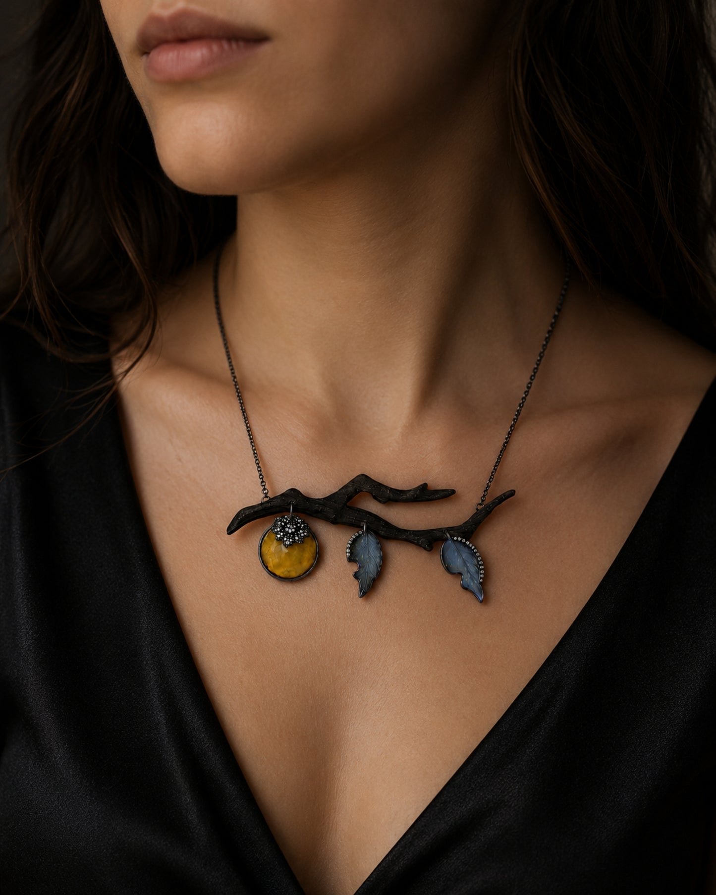Luxury persimmon branch pendant worn on model, handcrafted in ebony, black rhodium 18K white gold, diamonds, angelite, and golden lepidolite.