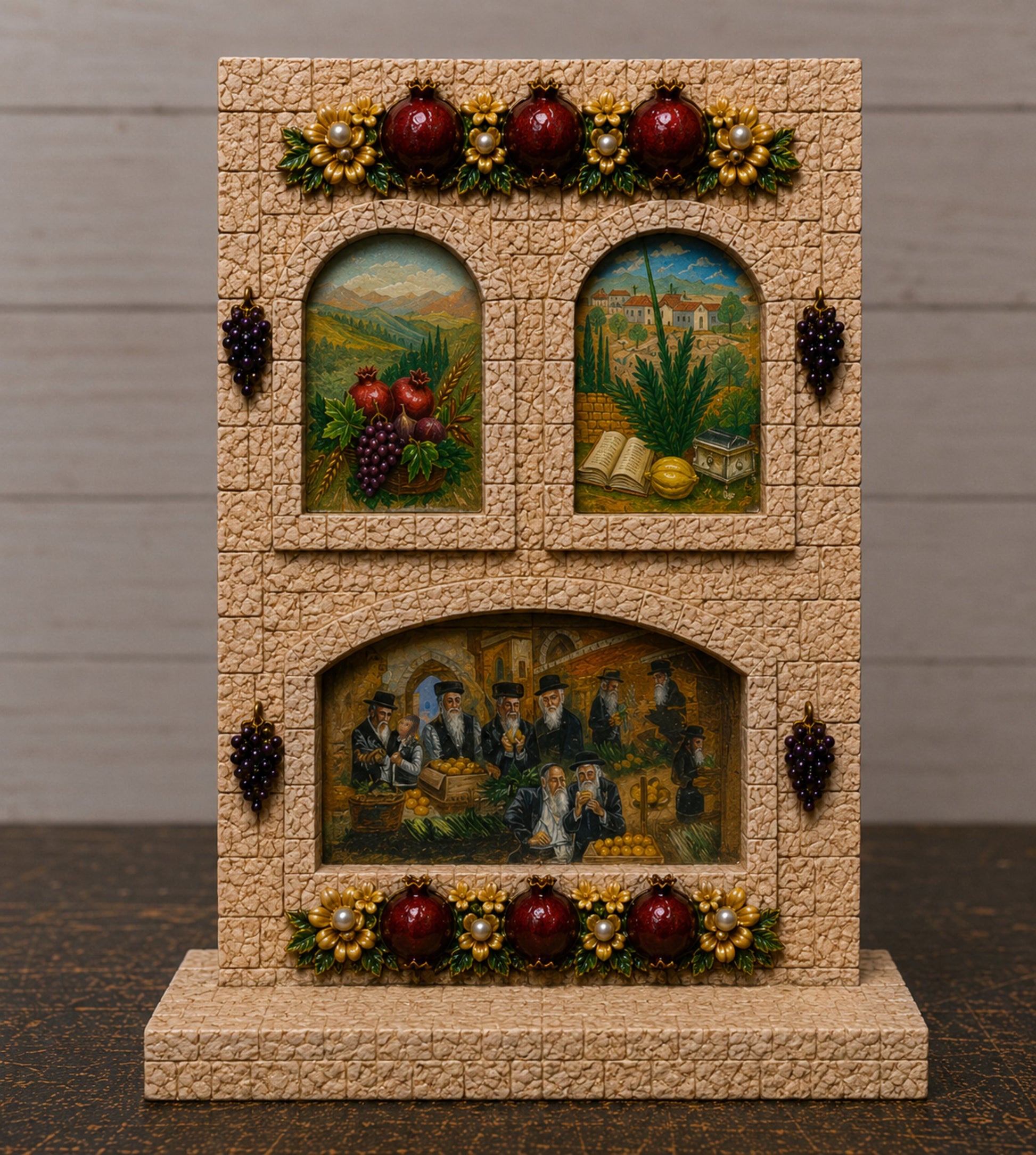A decorative tabletop display shaped like a stone wall with three arched windows showing painted scenes of grapes, wine, and a banquet, accented with red grapes, gold grapes, and dark grape clusters.