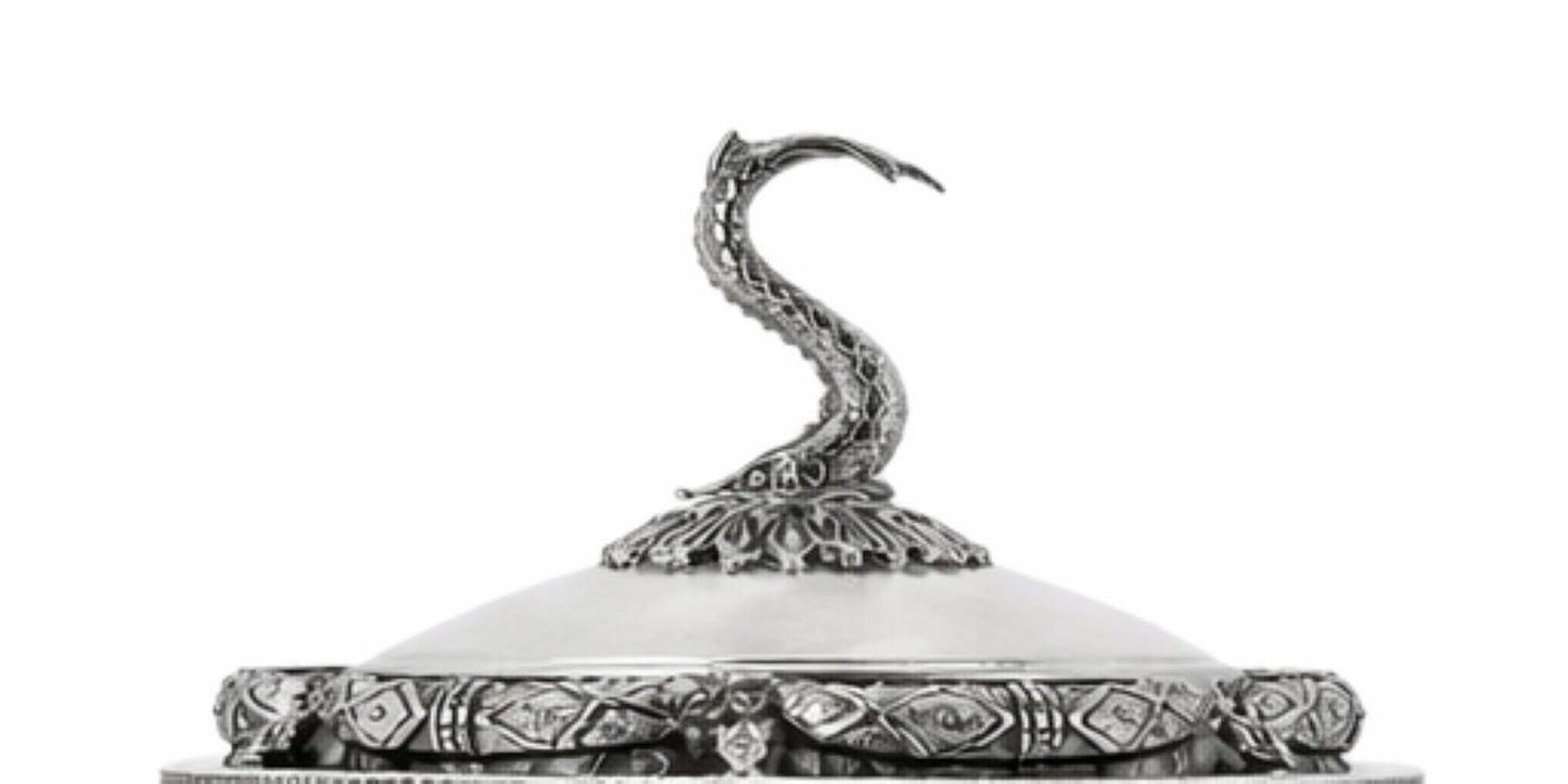 An ornate silver-toned metal container lid featuring a sculpted snake figure on top and a heavily decorated patterned rim, shown against a plain white background.