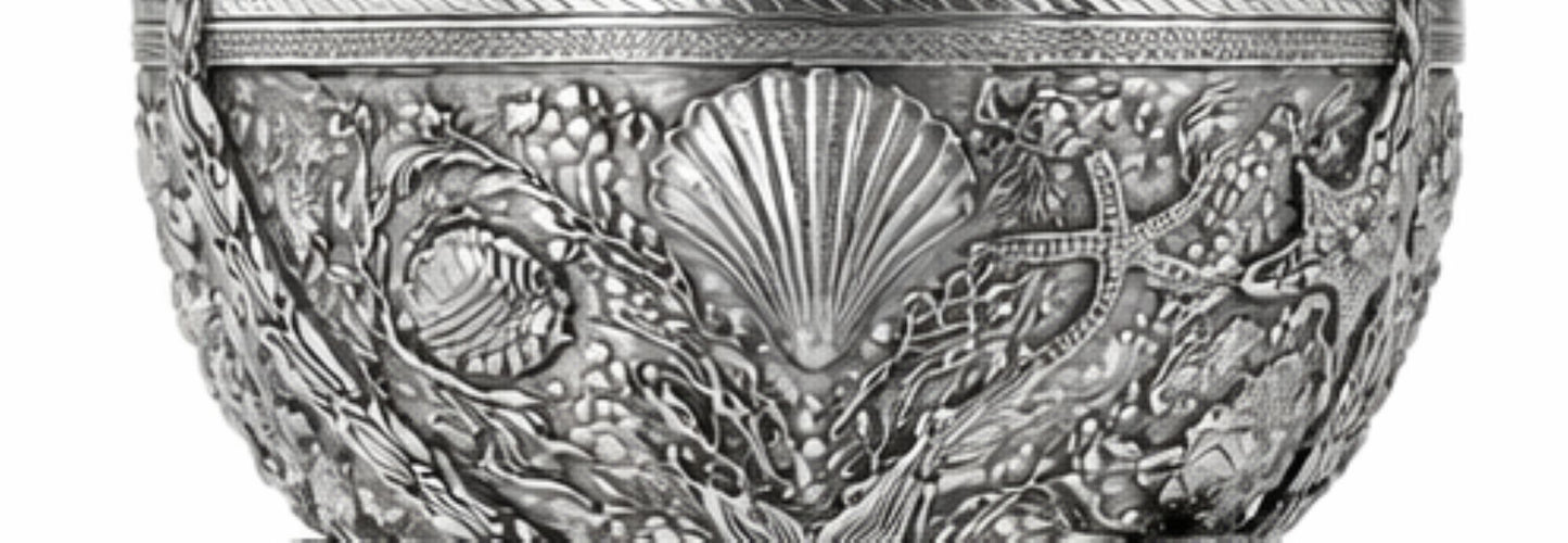An ornate silver-toned metal bowl featuring intricate embossed sea-themed relief patterns including a scallop shell, starfish, and coral.