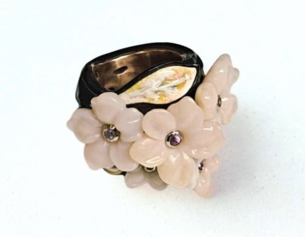 Pink Sakura ring by Konforti Jewelry, featuring hand-carved pink opal flowers set with 0.2 ct pink sapphires, 14K pink gold inner band, 18K yellow and white gold accents, hot enamel artwork, and ebony wood outer base from the Stone Garden Collection.