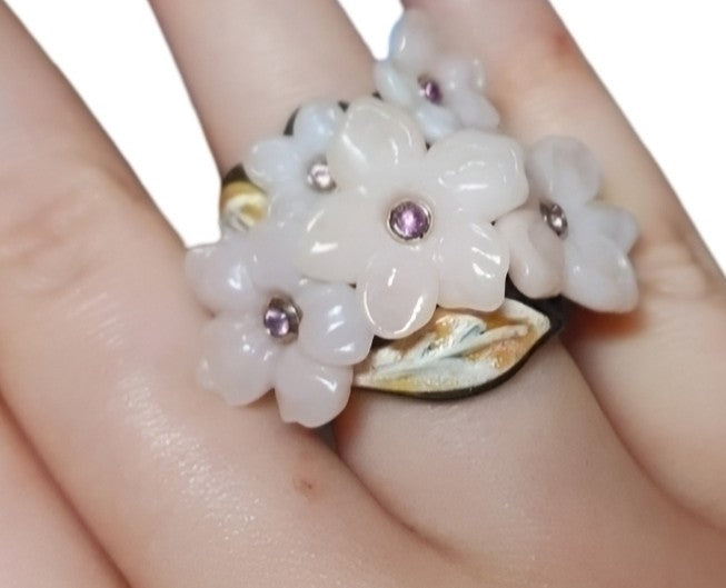 On-hand view of the Pink Sakura ring from the Stone Garden Collection, featuring hand-carved pink opal flowers with 0.2ct pink sapphires in 18K white gold, layered hot enamel over 18K yellow gold, a 14K pink gold inner base, and a black ebony outer ring.