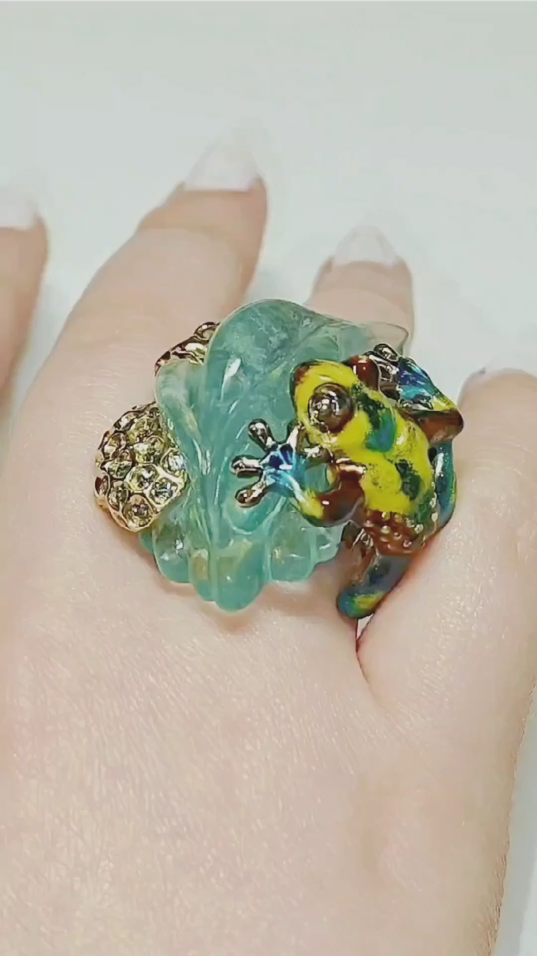 Video of the Summer Pond ring worn on the hand, featuring a hand-carved 64ct aquamarine gemstone in 18K yellow gold. The clip shows the gemstone’s depth, the vivid hot enamel painting inspired by Limoges techniques, and the 4.5ct multicolor sapphires that enhance the ring’s brilliance as it moves in the light.