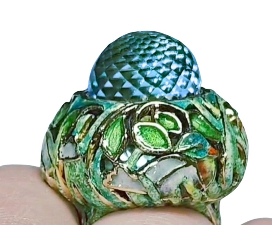 Close-up on-hand view of the Shimmering Pond ring in 18K yellow gold, highlighting the 33.3ct Swiss topaz briolette and the detailed Champlevé hot enamel artwork from the Stone Garden Collection.