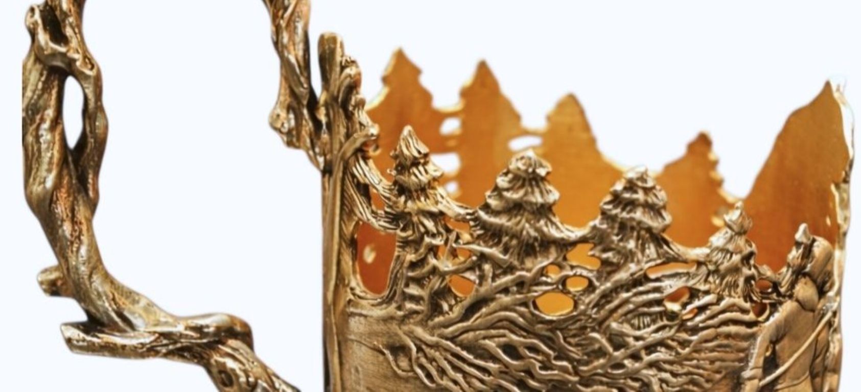 Close-up of sterling silver cup holder showing detailed winter forest relief with pine trees, moving figures, animals, and flowing snow landscape in narrative sculptural design