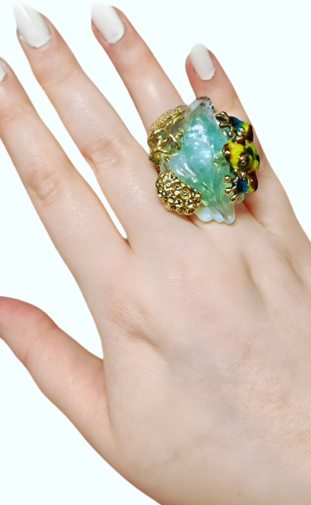 Hand shot of the Summer Pond ring from a frontal angle, highlighting the carved 64ct aquamarine centerpiece, layered enamel artwork, and sapphire details in 18K yellow gold.
