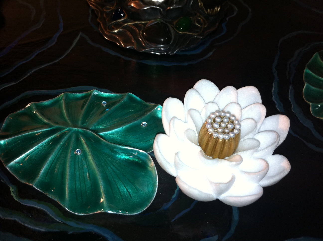 Top view detail of the “Summer Pond” monumental sculptural centerpiece, featuring a hand-carved chalcedony flower with pearl inlays resting on a silver lily pad, surrounded by transparent hot enamel over guilloché that recreates the shimmering surface of water.