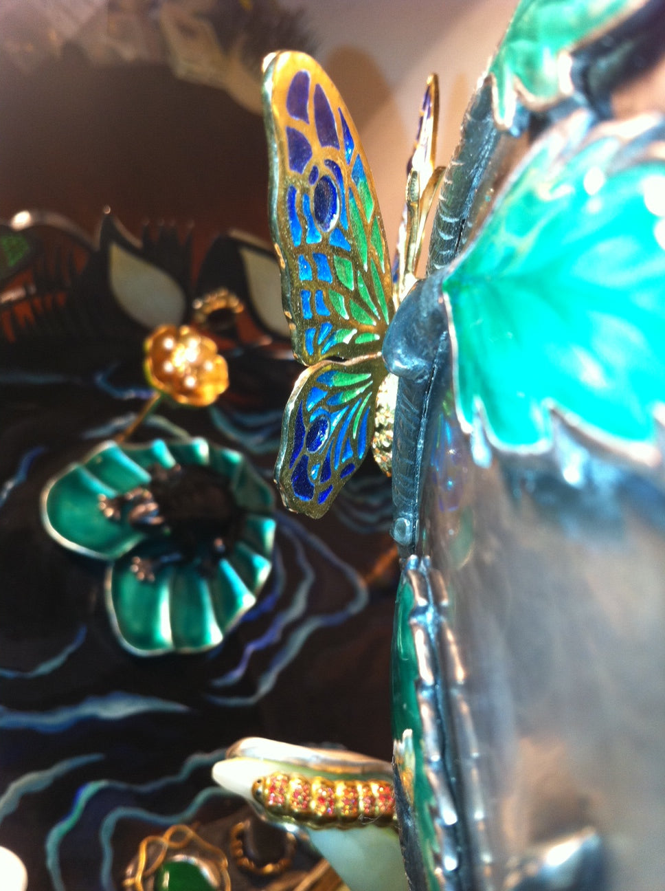 Sculptural detail of the “Summer Pond” centerpiece showing a silver frog perched on a lily pad with a hand-carved gemstone flower, enhanced with hot enamel and traditional jewelry-setting techniques.