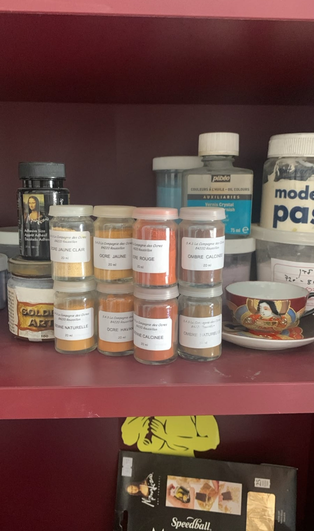A shelf display of various spice jars and containers, including a prominent white jar labeled 'model paste' and several smaller spice jars with white labels, set against a dark red shelving unit.
