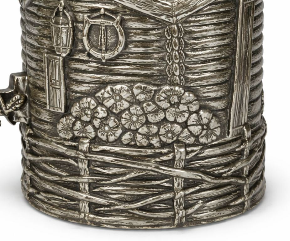 Close-up of sterling silver narrative cup holder featuring floral relief, woven fence motif, countryside textures, and handcrafted silversmith engraving